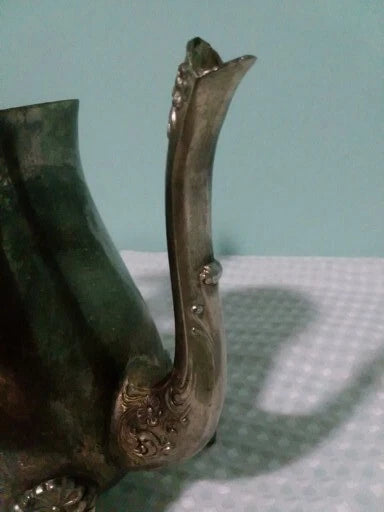 Decorative metal teaspout on a te pot textured surface with a light blue background