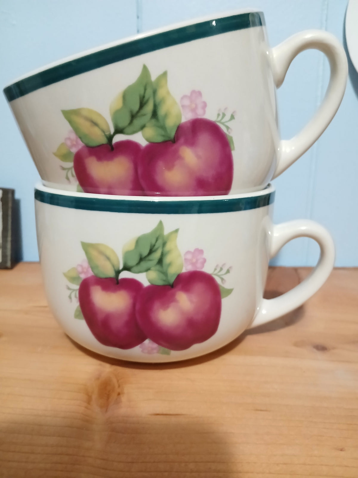 Two ceramic mugs with apple design on a wooden surface