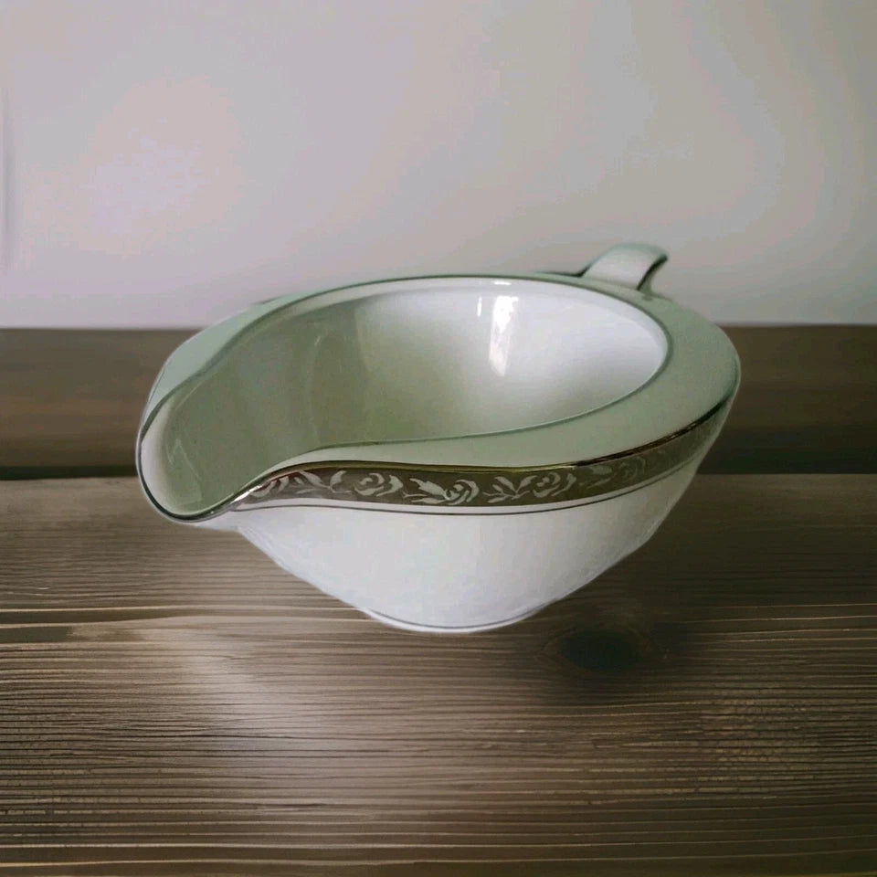 White ceramic gravy boat with green rim and decorative band on a wooden surface
