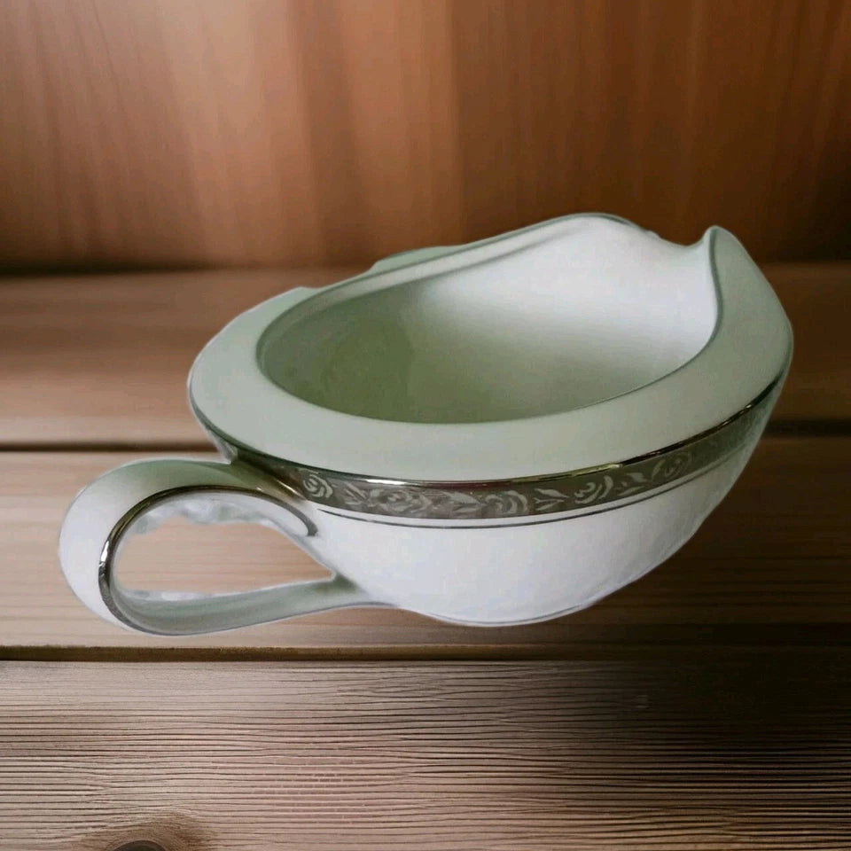 Decorative white gravy boat with silver handle on a wooden surface
