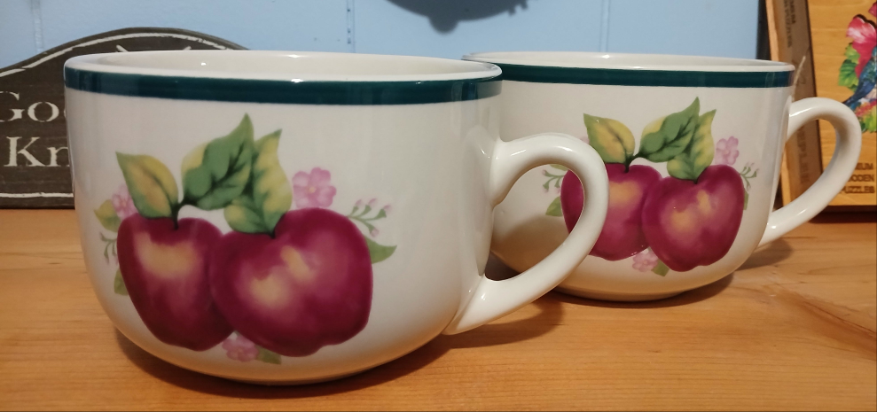 Two ceramic mugs with apple design on a wooden surface