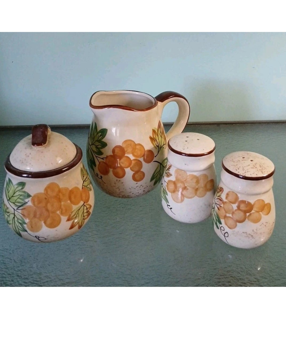 Set of four ceramic jars with grape design on a glass surface