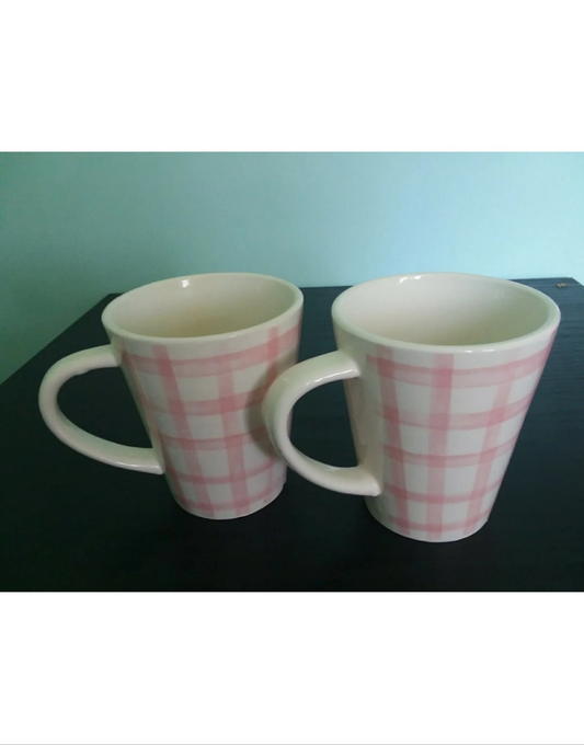 Two white mugs with pink checkered patterns on a black surface.