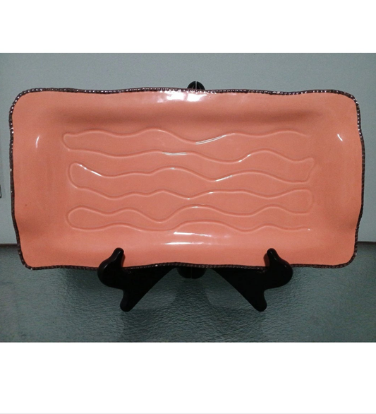 Pink ceramic tray with wavy design on a black stand against a gray background