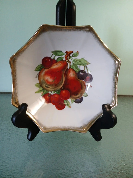 Decorative plate with fruit design on a stand against a light green background