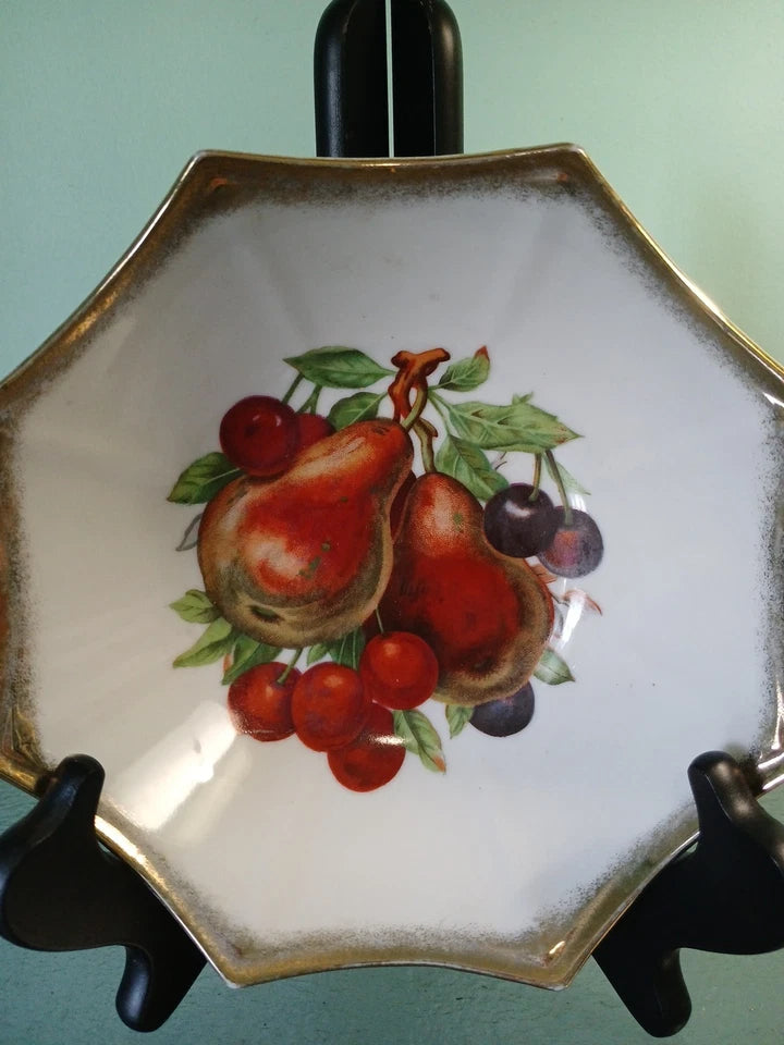 Decorative plate with fruit design on a stand against a light green background