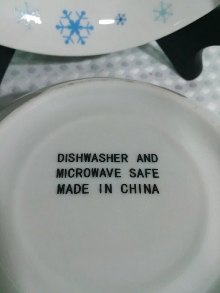 White plate with blue snowflake designs and text indicating dishwasher and microwave safety, made in China.