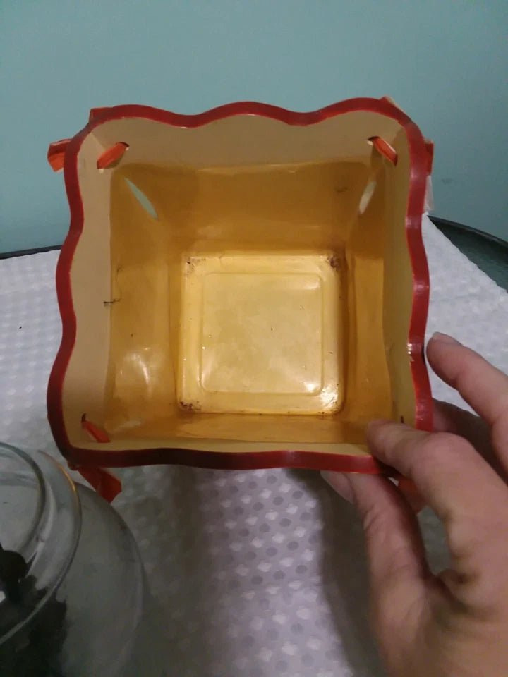 Hand holding a yellow square bowl with red rim on a light blue background