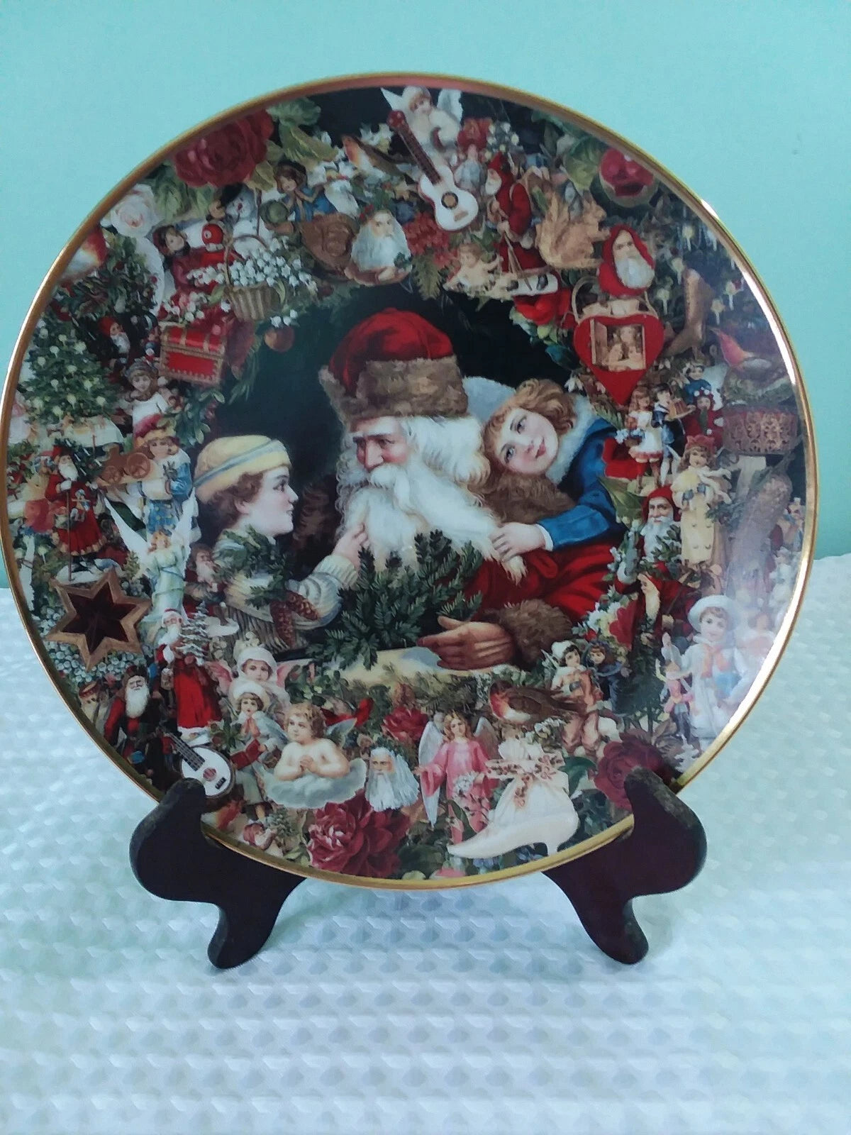 Decorative Christmas plate with Santa Claus and other holiday characters on a stand against a light blue background.