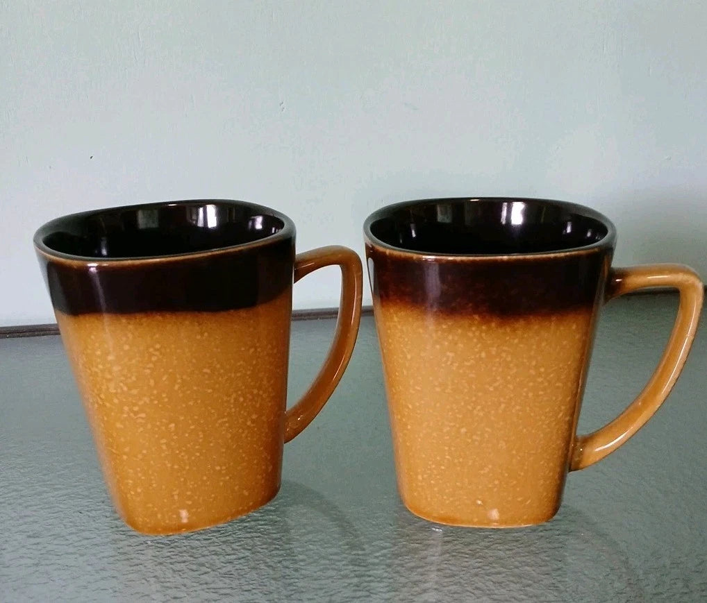 Two brown ceramic mugs with black rims on a glass surface.