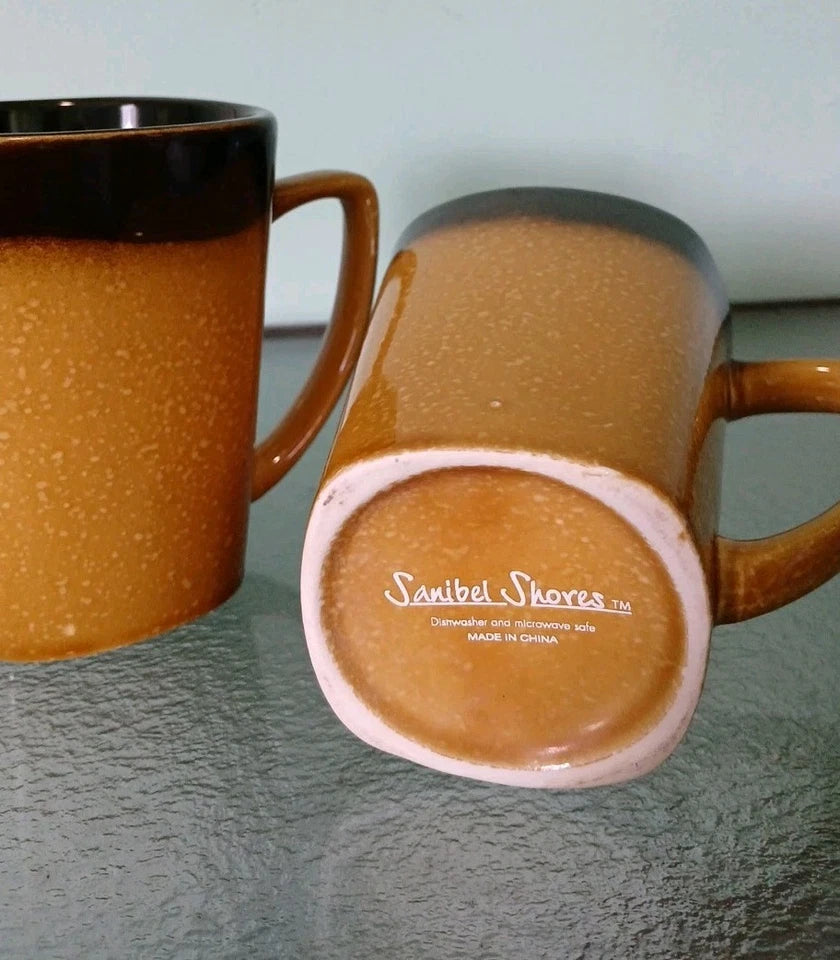 Two brown ceramic mugs with a visible brand logo on a gray surface.