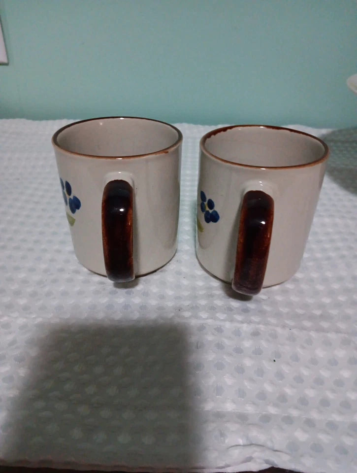 Two ceramic mugs with brown handles on a textured surface.