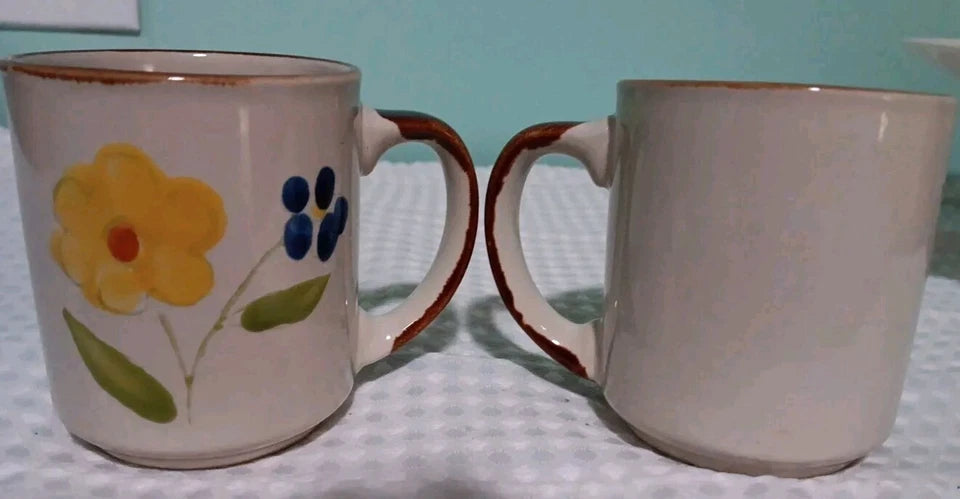 Two ceramic mugs with floral design on a textured surface.