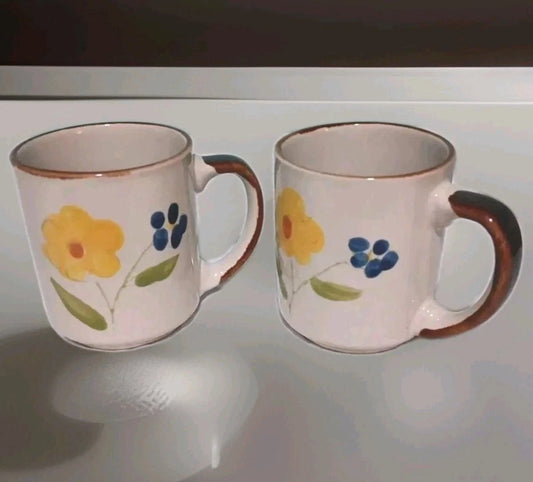 Two ceramic mugs with floral designs on a reflective surface.