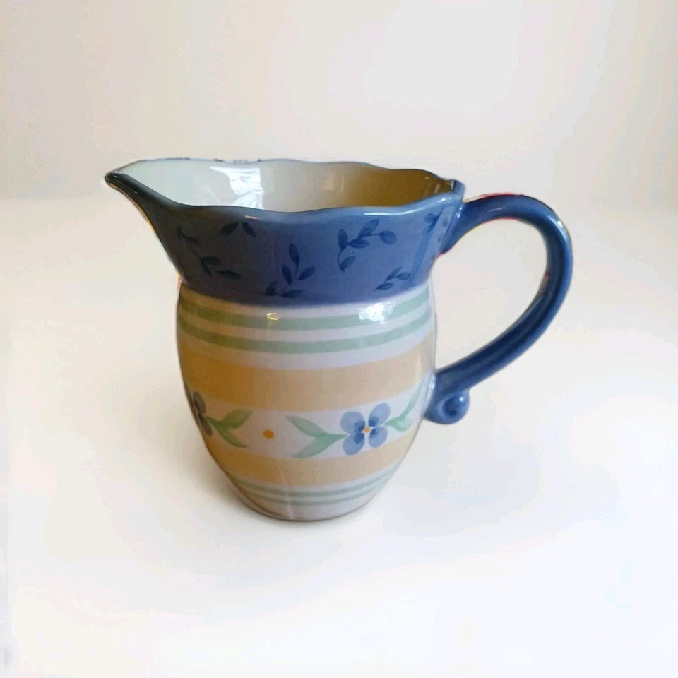 Ceramic pitcher with blue top and floral patterns on a white background