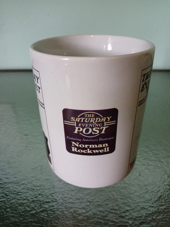 White mug with 'The Saturday Evening Post' and Norman Rockwell branding on a green surface.