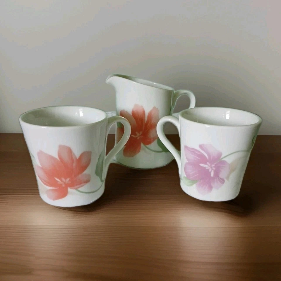 Two floral mugs and a pitcher on a wooden surface with a neutral background