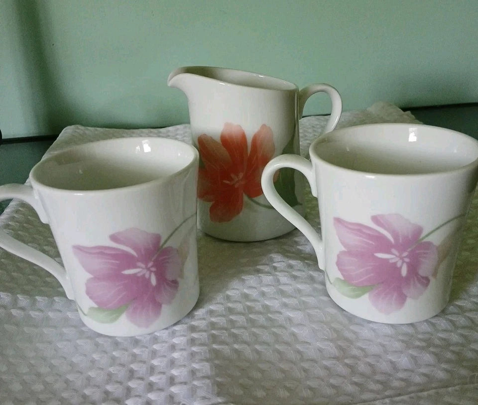 Two mugs and a pitcher with floral designs on a textured surface.