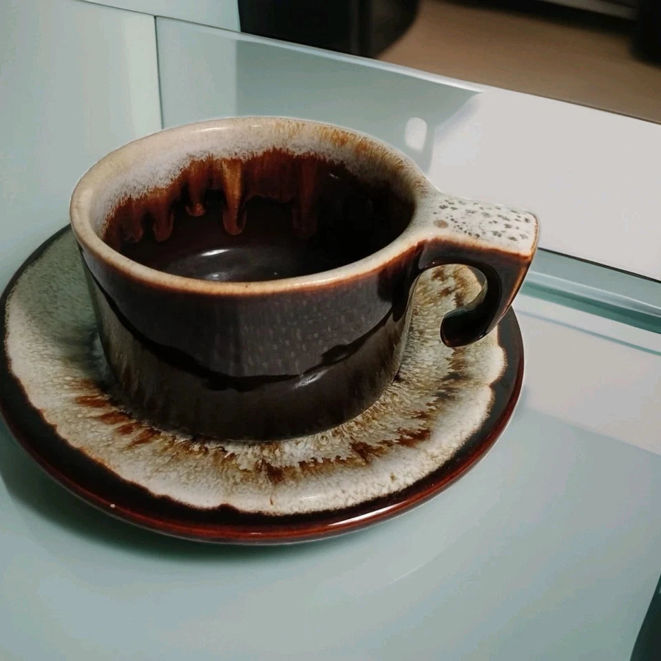 Ceramic cup and saucer with a textured finish on a reflective surface.