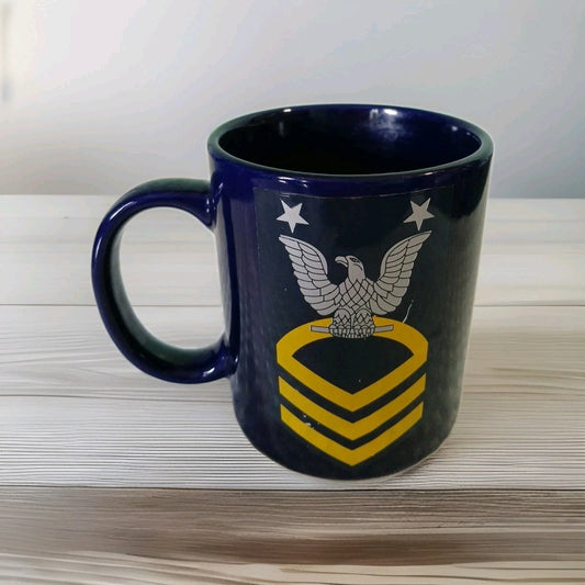 Navy blue mug with an eagle emblem and yellow chevrons on a light wooden surface.