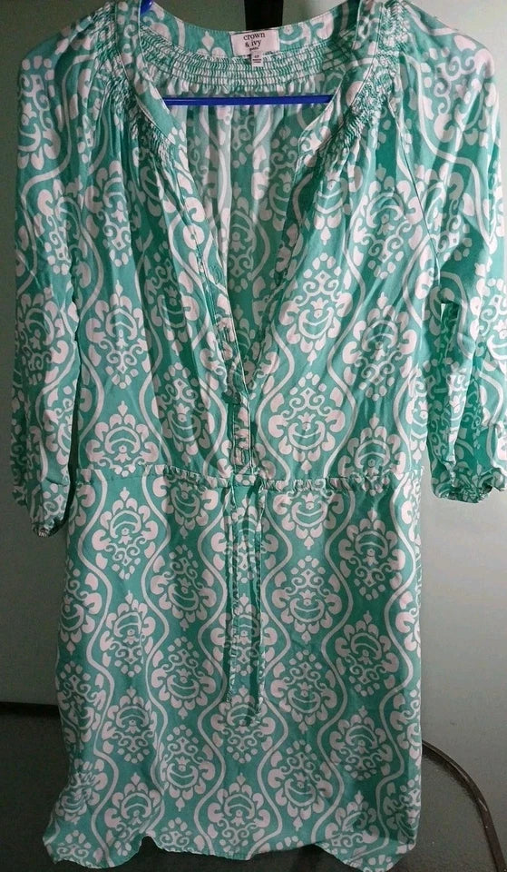 Green and white patterned dress on a hanger against a white background