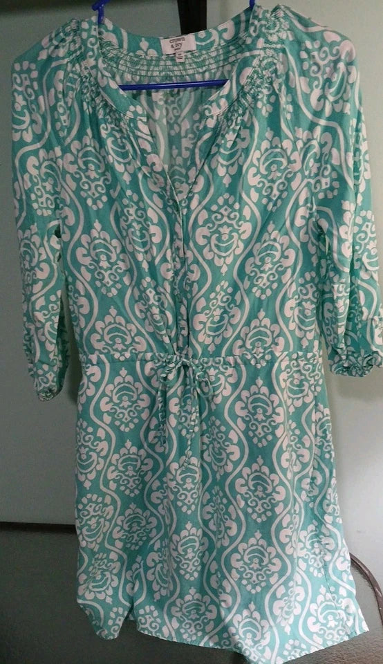 Teal and white patterned dress on a hanger against a neutral background