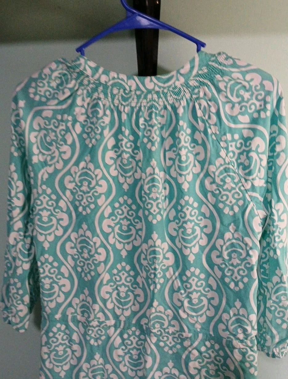 Teal and white patterned blouse on a hanger against a neutral background