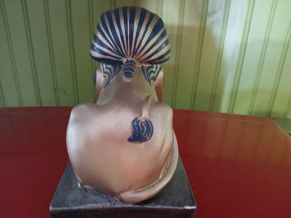 Mannequin head with stylized hair and neck tattoo on a red surface with green striped wallpaper.
