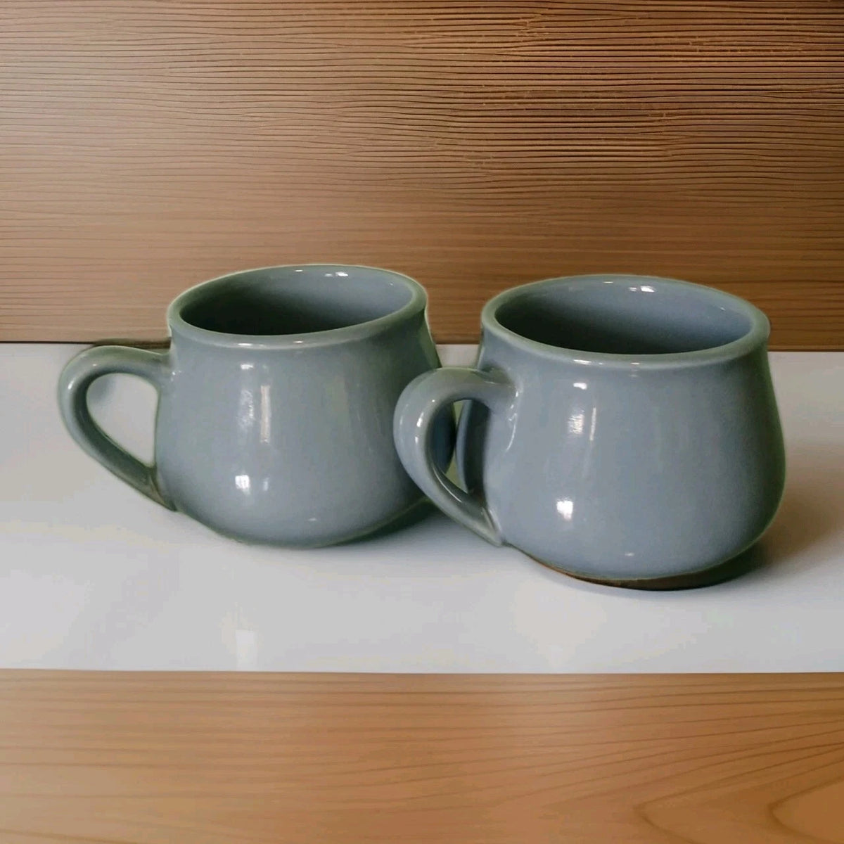 Two gray ceramic mugs on a white surface with a wooden background