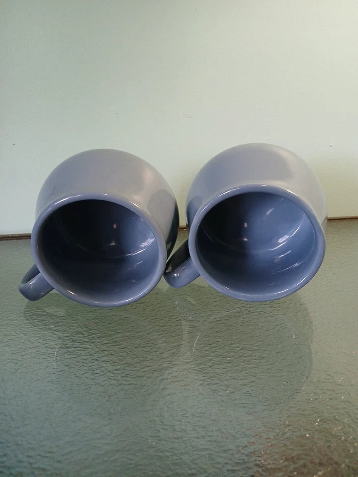 Two blue mugs on a reflective surface with a light green background