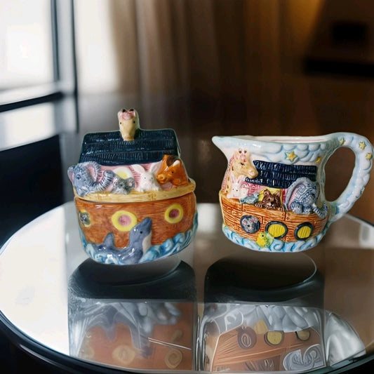 Two ceramic items resembling Noah's Ark on a reflective surface with a blurred background.