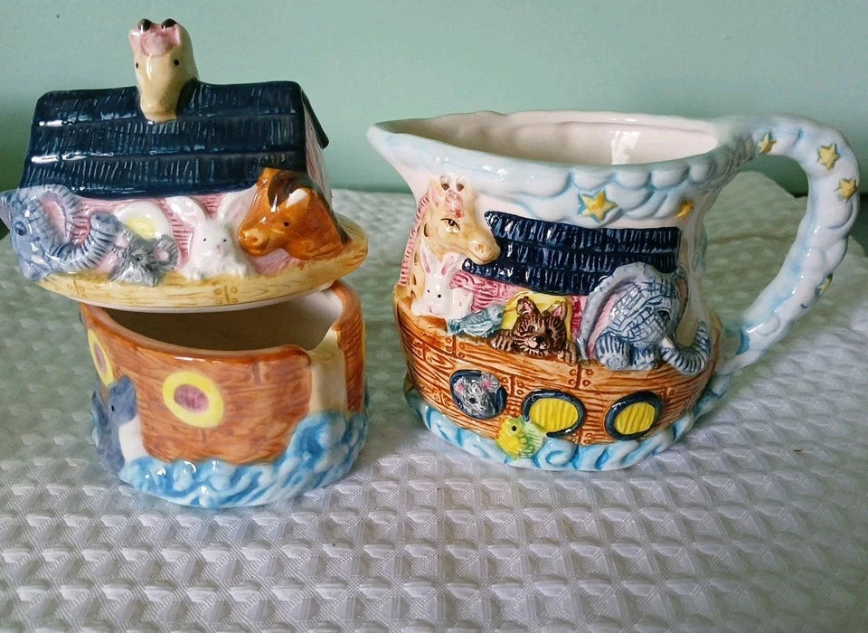 Two ceramic items, a Noah's Ark-shaped container and a pitcher with animal designs, on a textured surface.