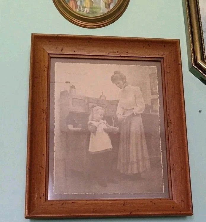 Framed black and white photograph of a woman and child on a light green wall.