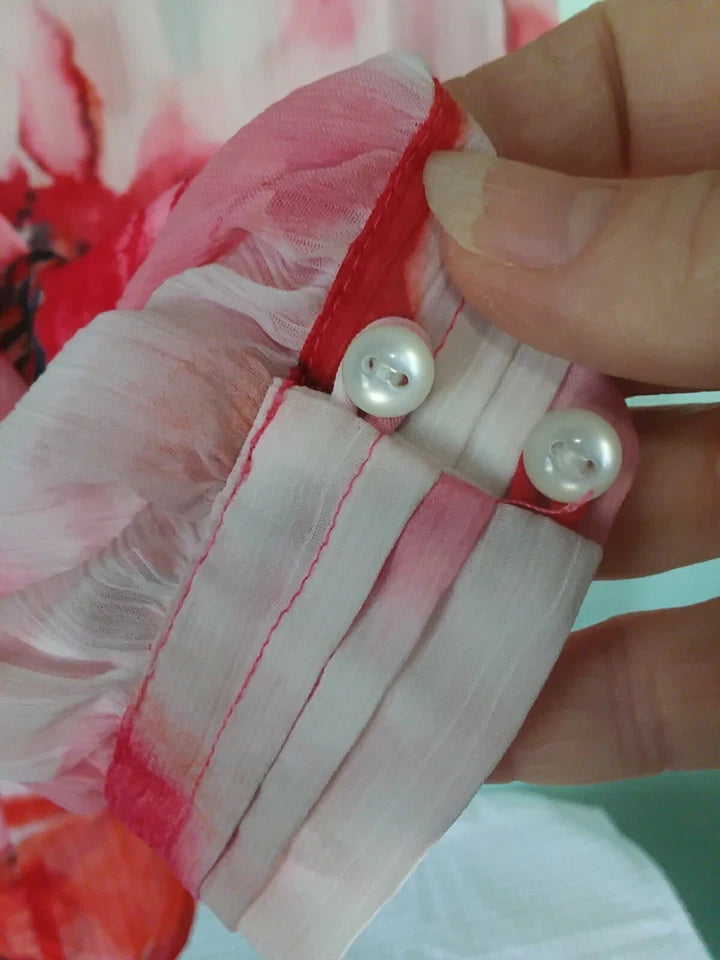 Close-up of a hand holding a red object with pearl-like beads against a floral background.
