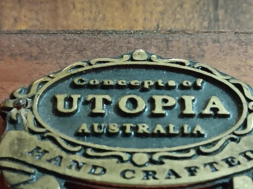 Brass plaque with 'Concepts of Utopia Australia' text on a wooden background
