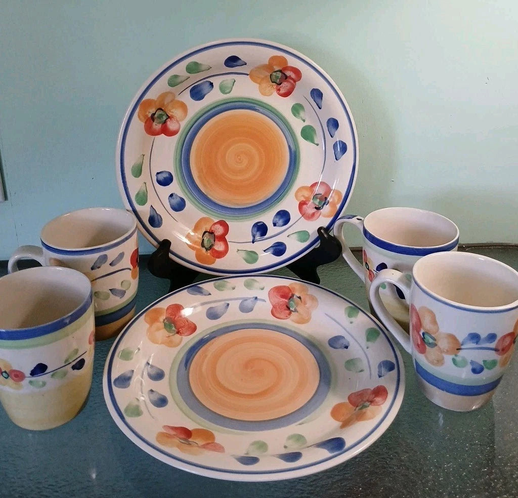 Set of ceramic plates and mugs with floral and spiral design on a green surface.