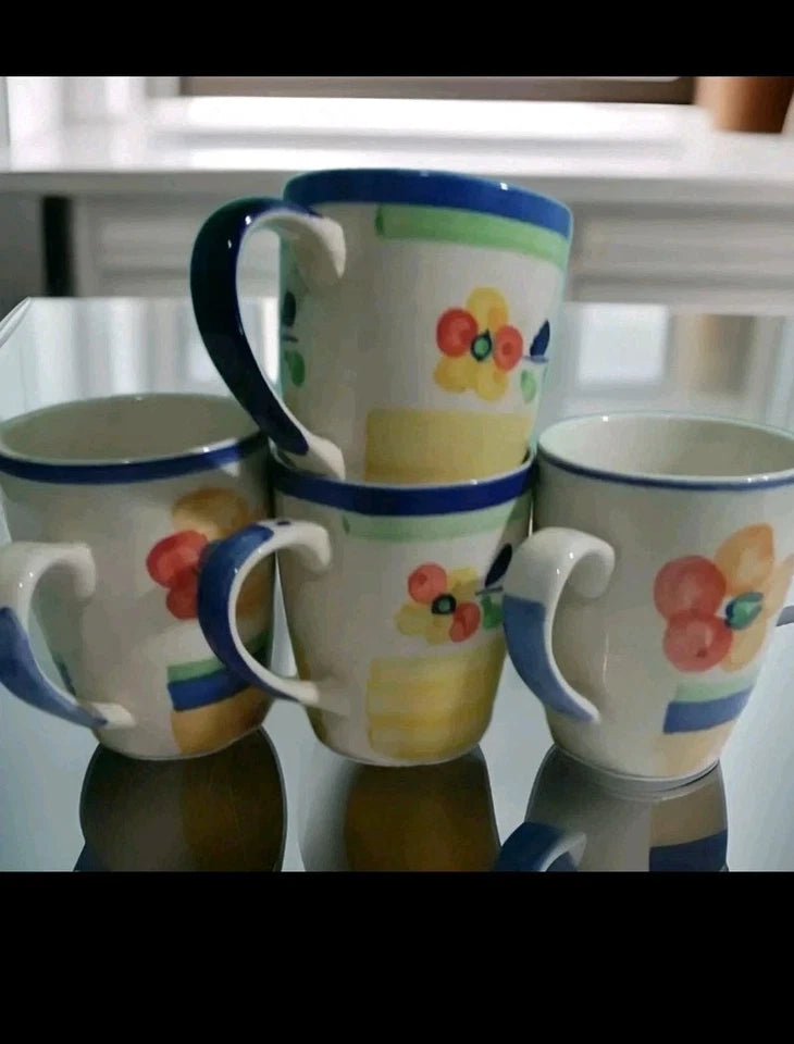 Set of four ceramic mugs with floral designs on a reflective surface.