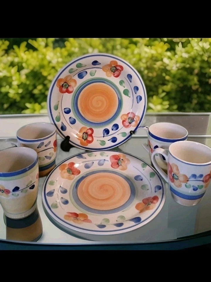 Set of ceramic plates and cups with floral patterns on a glass table.