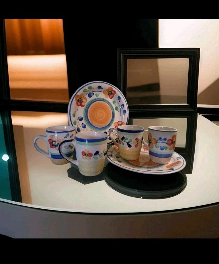 Set of ceramic cups and saucers with floral patterns on a reflective surface.