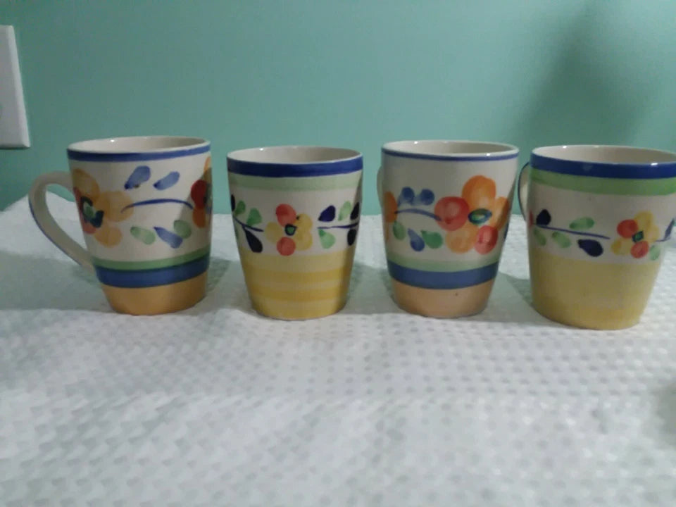 Four ceramic mugs with floral designs on a textured surface.
