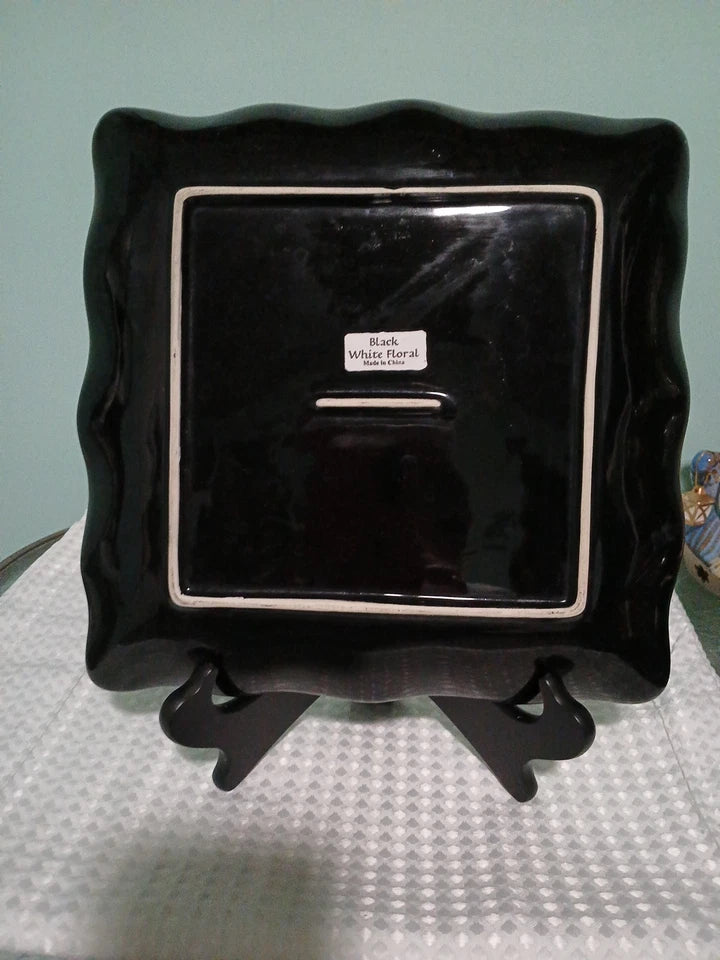 Black ceramic plate with silver rim on a stand against a light blue background