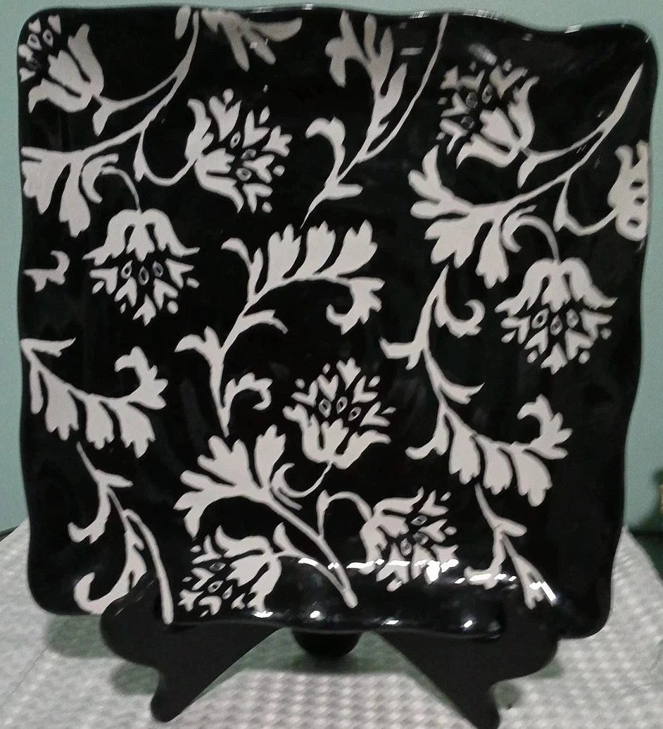 Black square plate with white floral pattern on a stand against a light blue background