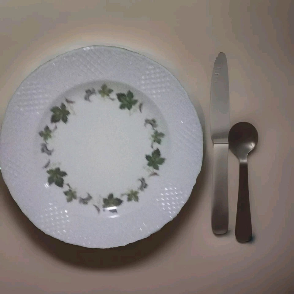 White plate with green leaf pattern, knife, and spoon on a beige background