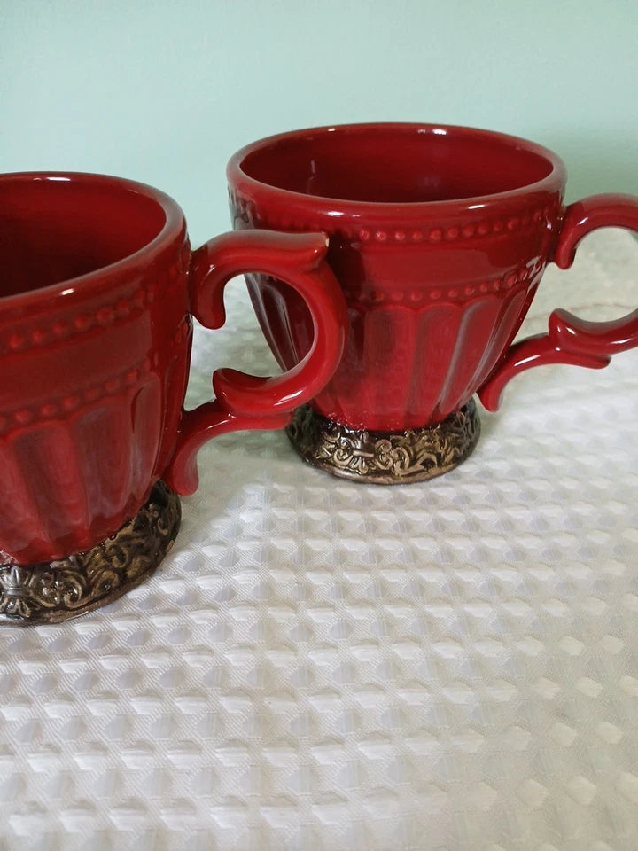 Two red mugs with decorative bases on a textured surface