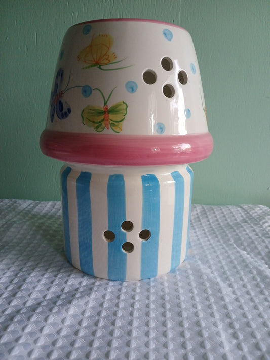 Decorative ceramic candle holder with blue and white stripes and pink top on a textured surface.