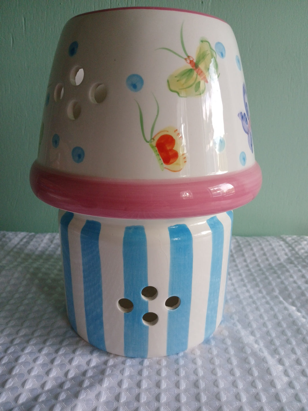 Ceramic candle holder with floral design and striped pattern on a textured surface.