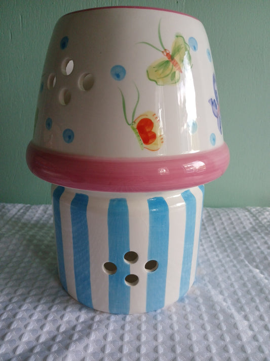 Ceramic candle holder with floral design and striped pattern on a textured surface.