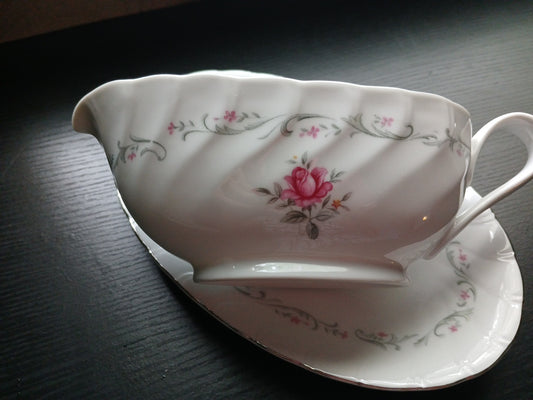 Ceramic gravy boat and saucer with floral design on a dark surface