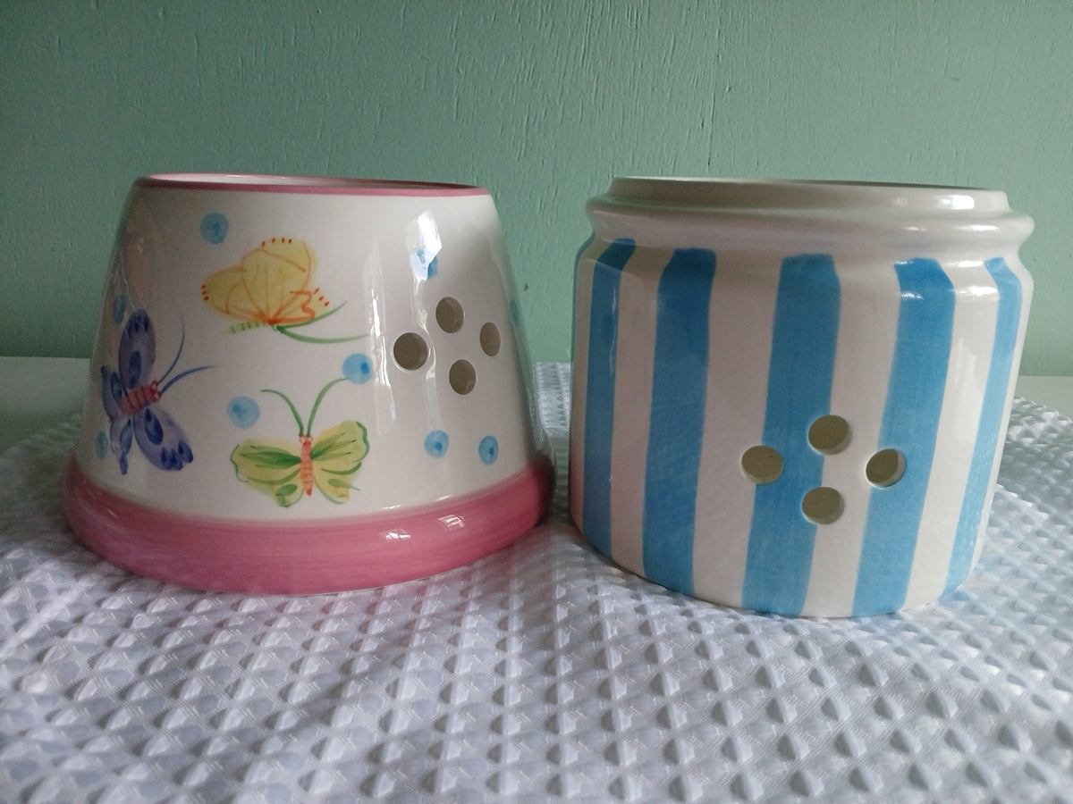 Two ceramic candle holder, one with blue stripes and the other with butterfly designs, on a textured surfac