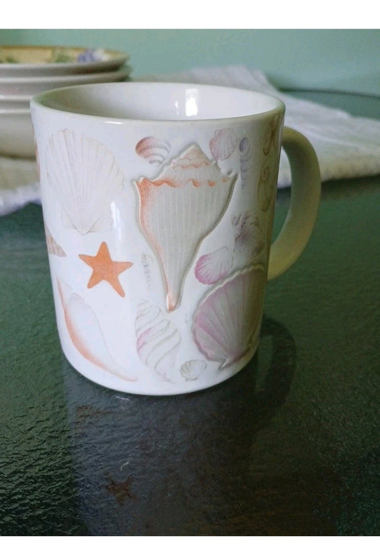 White mug with shell and starfish design on a dark surface